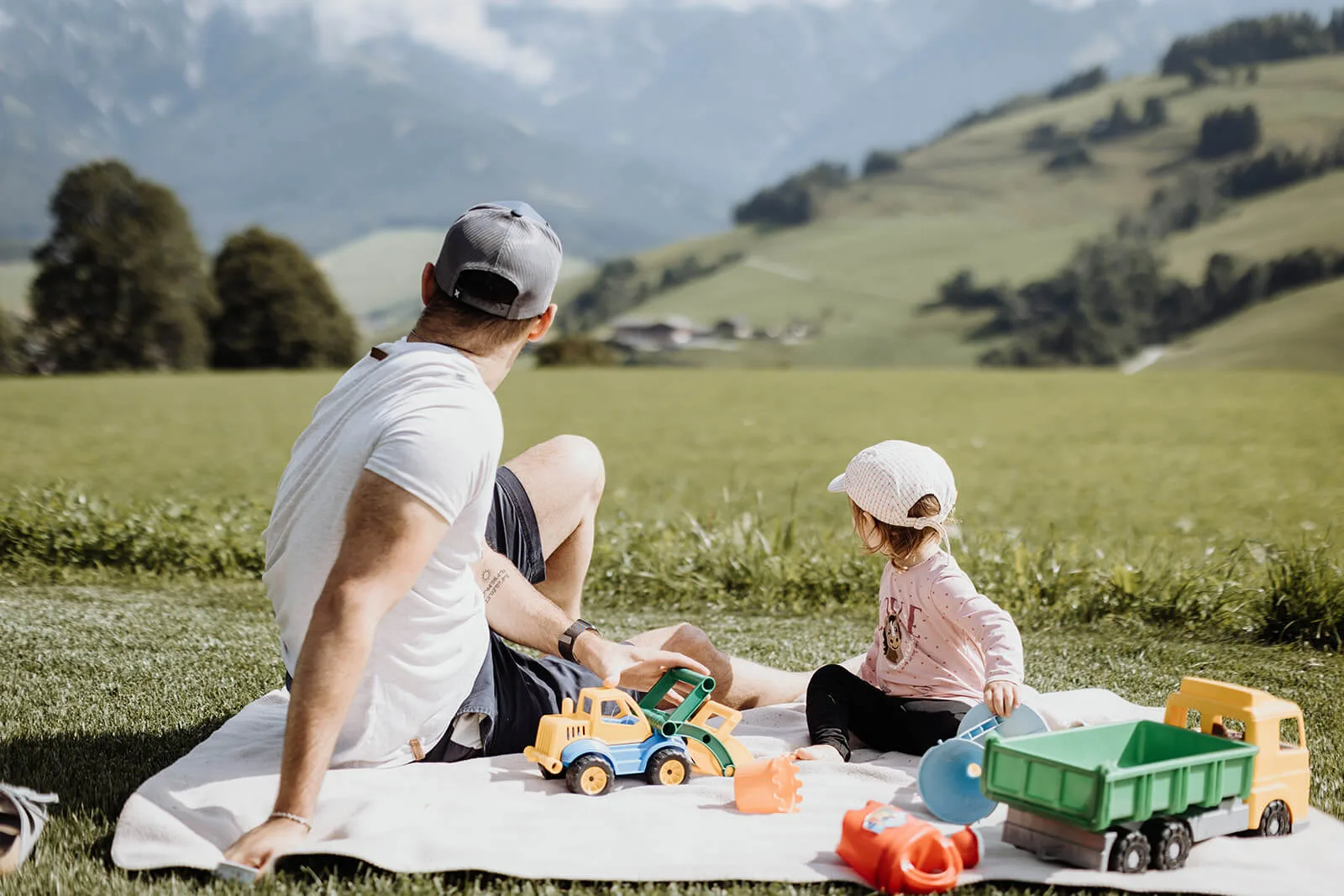 vater und tochter sitzen im gras und spielen am spielplatz am ebengut